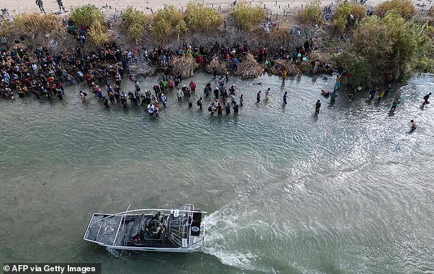 قارب دورية الحدود الأمريكية يمر بمجموعة كبيرة من المهاجرين الذين ينتظرون عبور حاجز الأسلاك الشائكة إلى الولايات المتحدة، في إيجل باس، تكساس