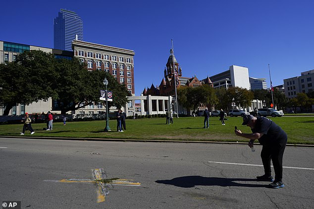 شخص يستخدم هاتفًا خلويًا لالتقاط صور لعلامة X في شارع Elm في Dealey Plaza