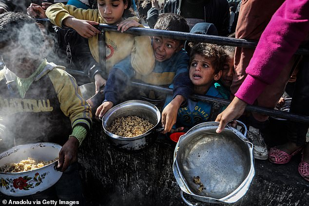 أطفال فلسطينيون ينتظرون في الطابور لتلقي الطعام الذي أعده المتطوعون للعائلات الفلسطينية، التي نزحت إلى جنوب غزة بسبب الهجمات الإسرائيلية، بين أنقاض المباني المدمرة في رفح، غزة في 9 فبراير.