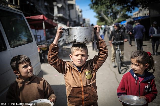 أطفال يحملون أدوات المطبخ وهم يسيرون نحو نقطة توزيع الغذاء في غزة