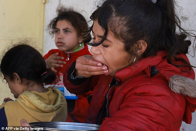 أطفال فلسطينيون نازحون يأكلون الأرز من وعاء بالقرب من نقطة توزيع المواد الغذائية في رفح، جنوب قطاع غزة، في 8 مارس