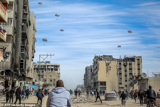 فلسطينيون يركضون في أحد الشوارع بينما يتم إسقاط المساعدات الإنسانية من الجو في مدينة غزة في 1 مارس 2024