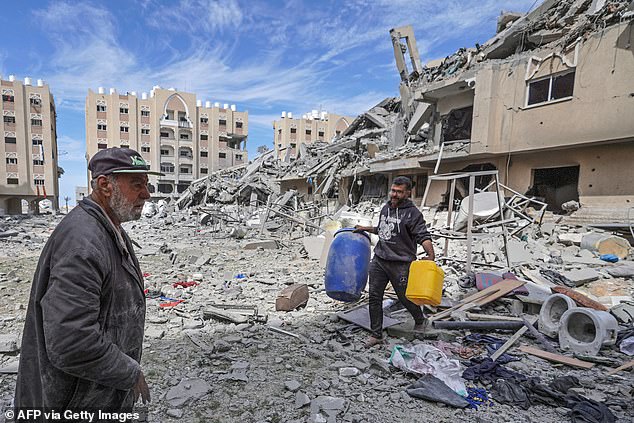 رجل فلسطيني نازح يحمل حاويات وسط أنقاض المنازل التي دمرها القصف الإسرائيلي في منطقة حمد غرب خان يونس جنوب قطاع غزة، 14 مارس 2024